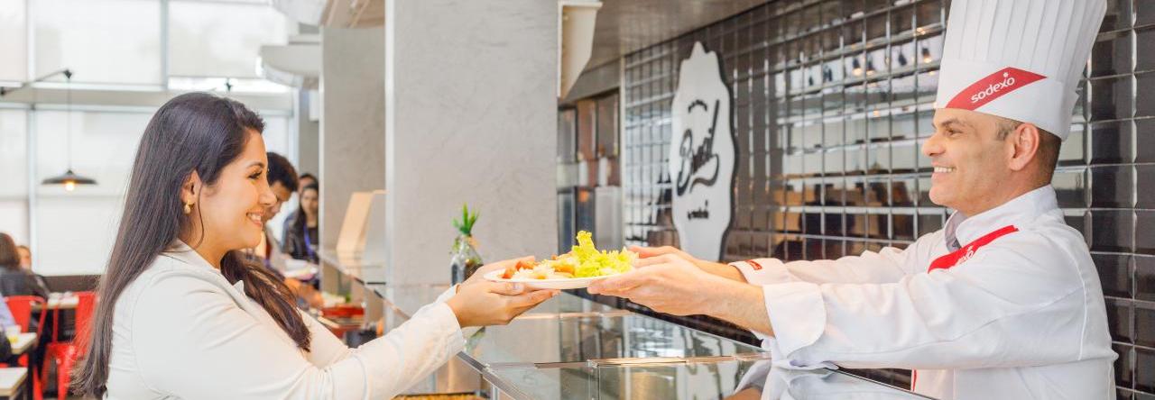 Chef de cozinha da Sodexo entrega comida à colaboradora em restaurante corporativo