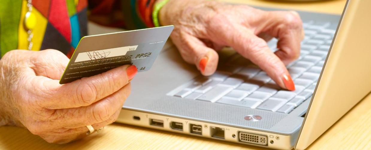 Mãos de uma idosa com cartão nas mão e no computador