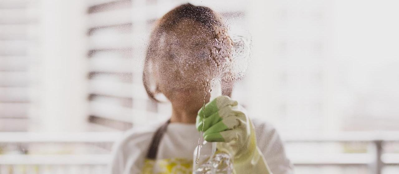Mulher com luvas limpa o vidro de casa com um pano e spray de álcool