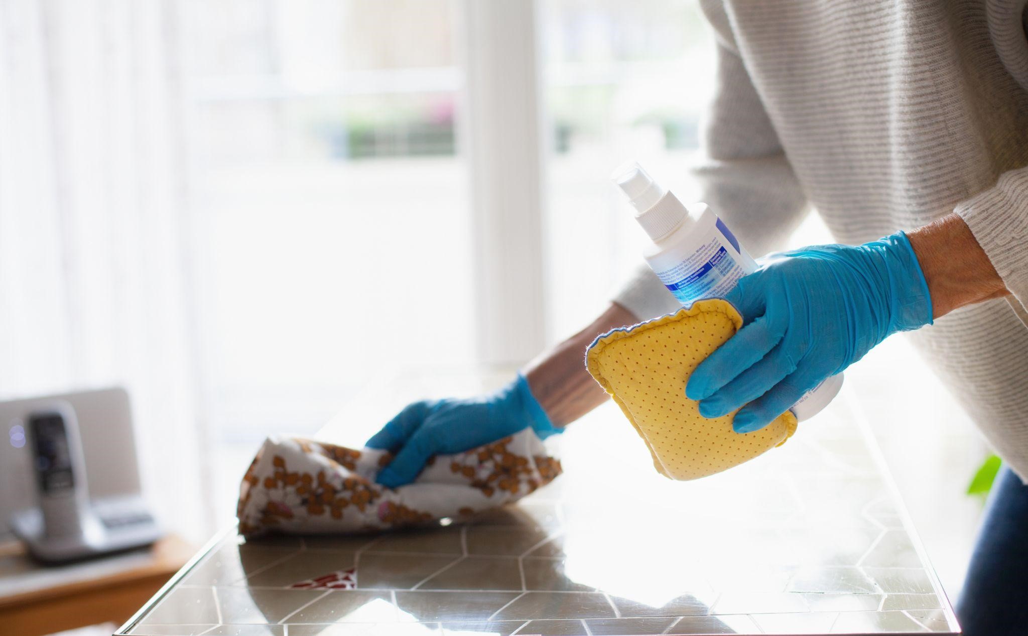 Pessoa higieniza e limpa superfície de casa