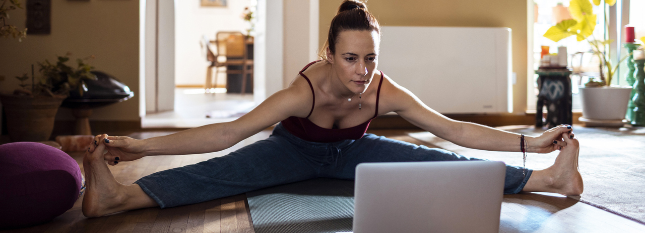 Mulher fazendo ioga em sua sala de casa com o auxilio de um computador