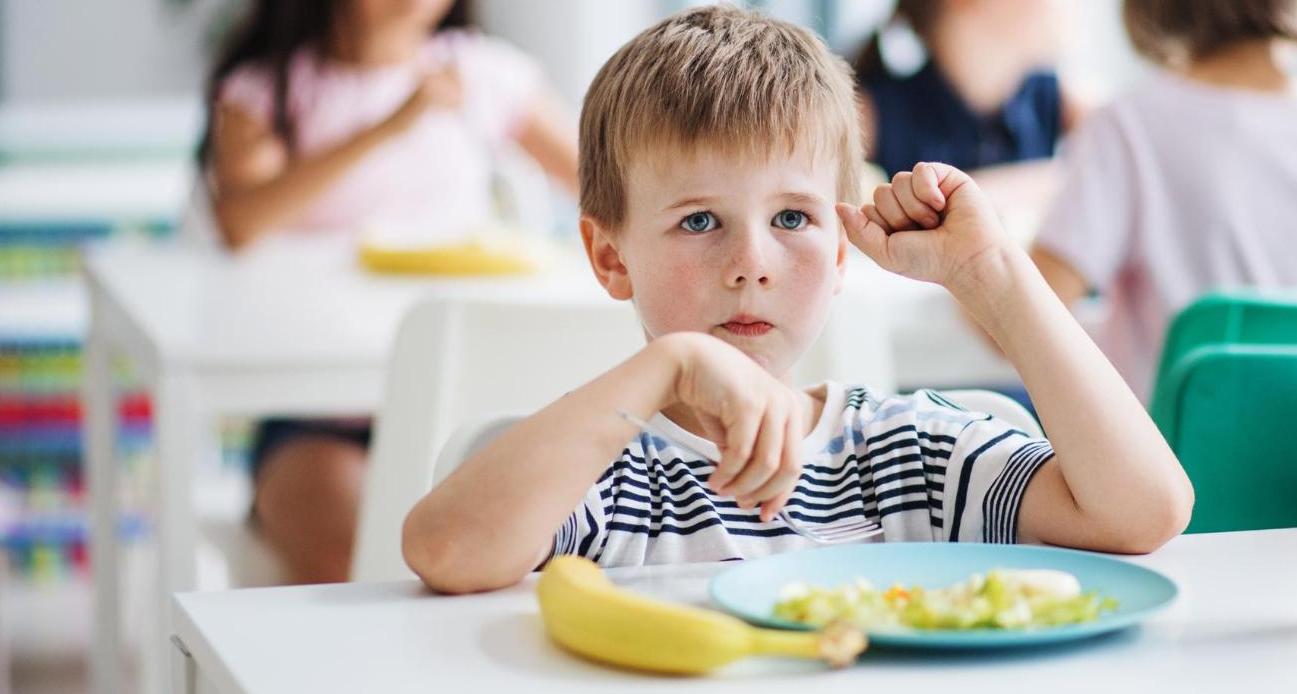 criança olha para câmera enquanto segura bandeja com prato em almoço na escola